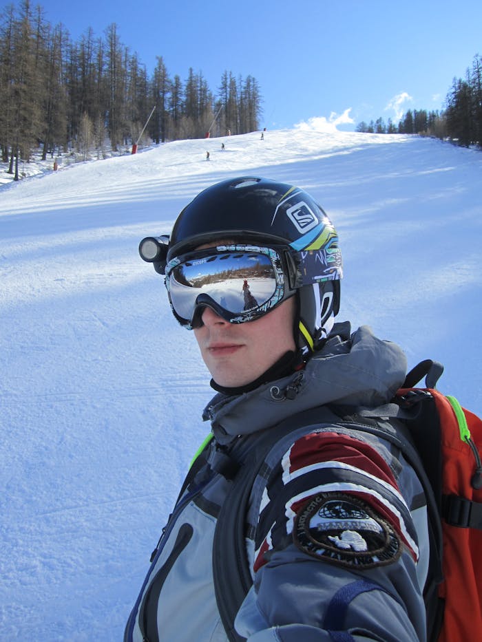 A skier poses with goggles and helmet on a sunny day at a ski resort.